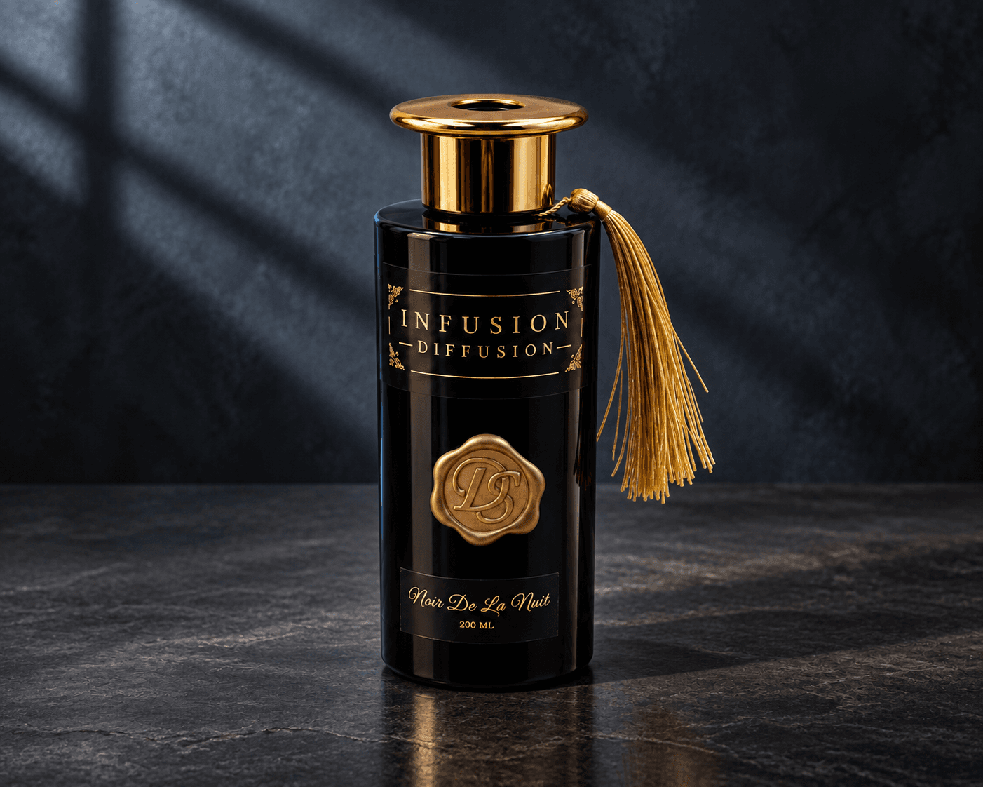 Noir De La Nuit black diffuser bottle with gold collar, seal and tassel on dark slate, lit by soft window shadows.